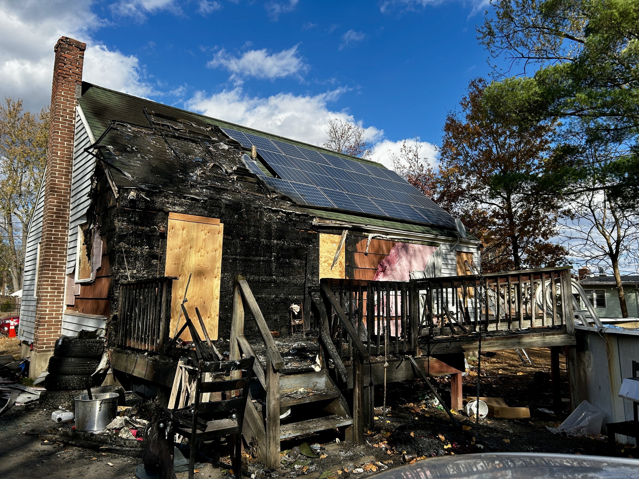 Fire damaged home exterior with charred siding and boarded windows